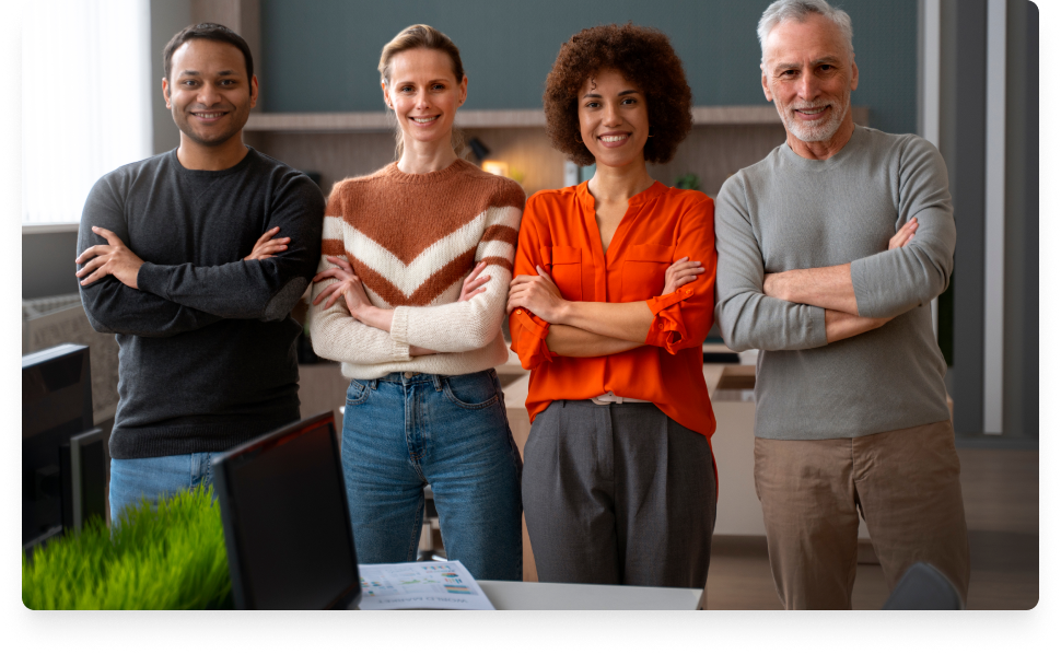 Dois homens e duas mulheres com braços cruzados sorrindo. Todos vestem calças e camisas e blusas de mangas compridas.
